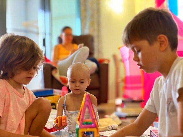 Child with cancer and her siblings playing together on the floor