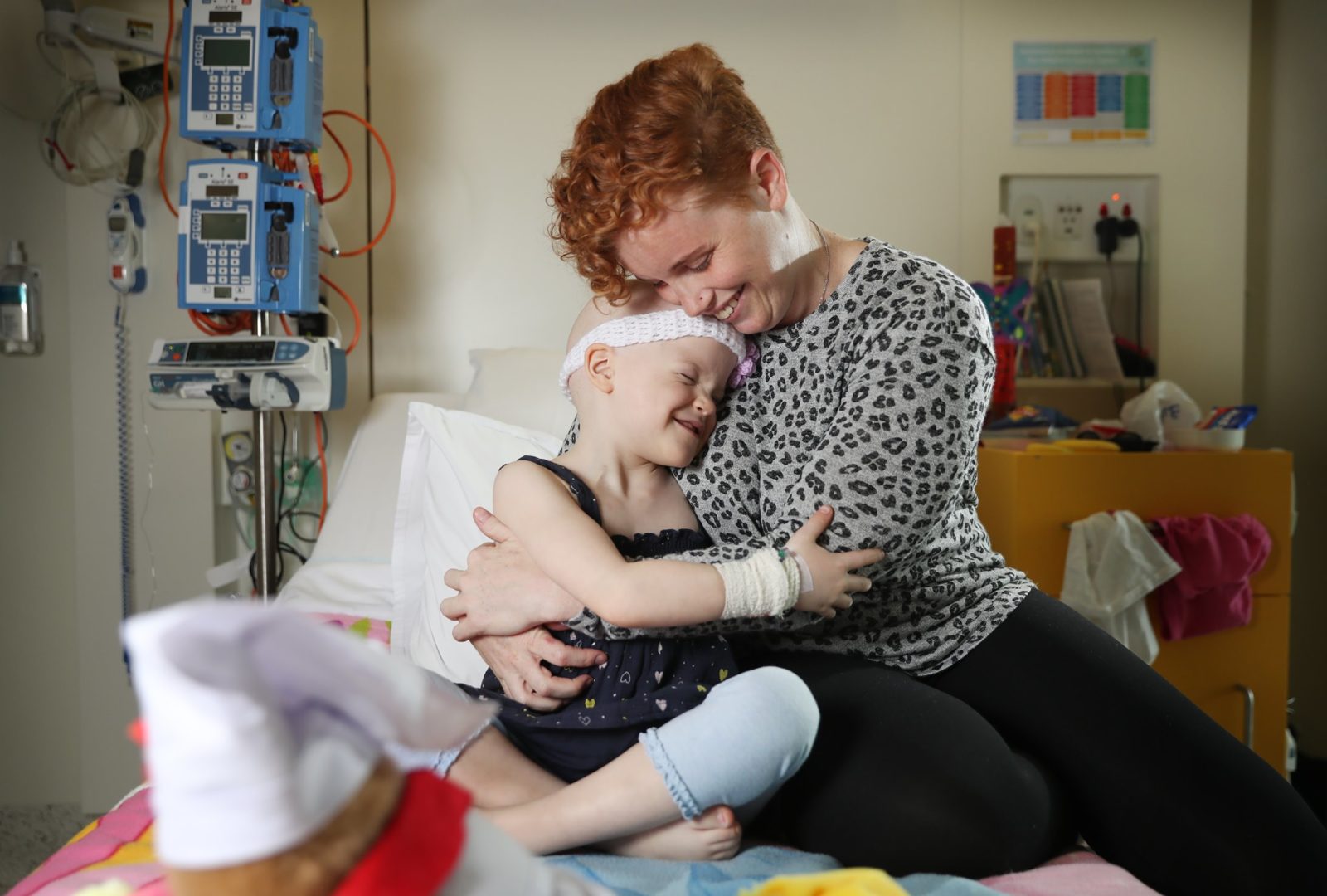 A mum hugging her daughter on a hospital bed.