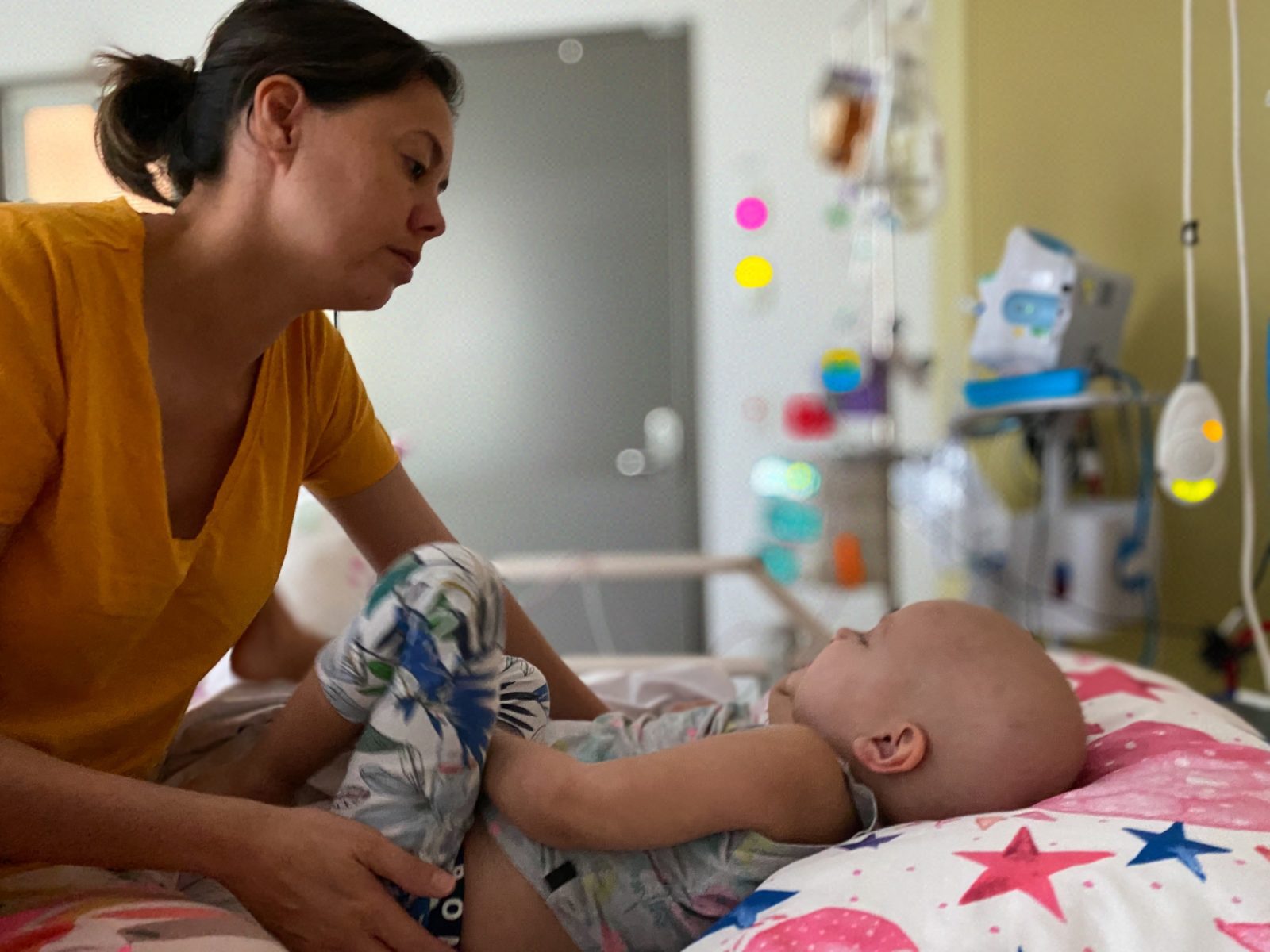 Mum leans over daughter, who has cancer, on a hospital bed.