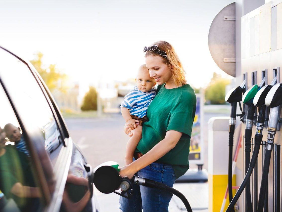 Woman holding a baby and putting petrol in her car